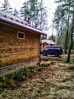 Здание с бордовой кровлей и системой водостока среди елей