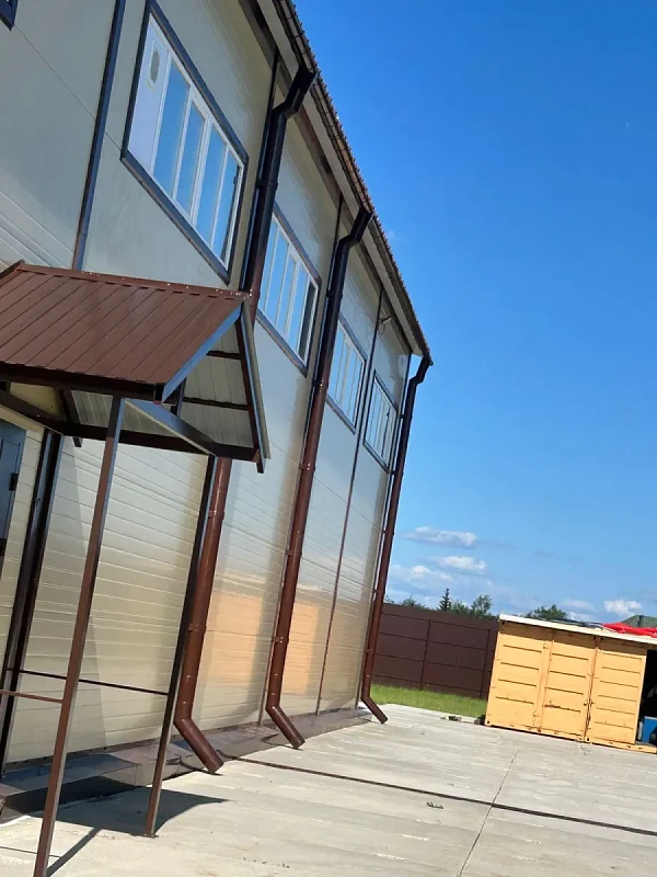 Двухэтажное здание с бежевым сайдингом и коричневым водостоком