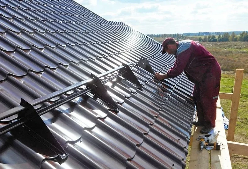 Монтажник устанавливает трубчатые снегозадержатели на крыше Монтажник устанавливает трубчатые снегозадержатели на крыше