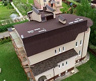 Процесс монтажа кровли коттеджа со строительными лесами