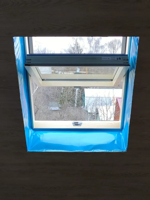 Установленное мансардное окно с деревянной рамой и синей пароизоляцией