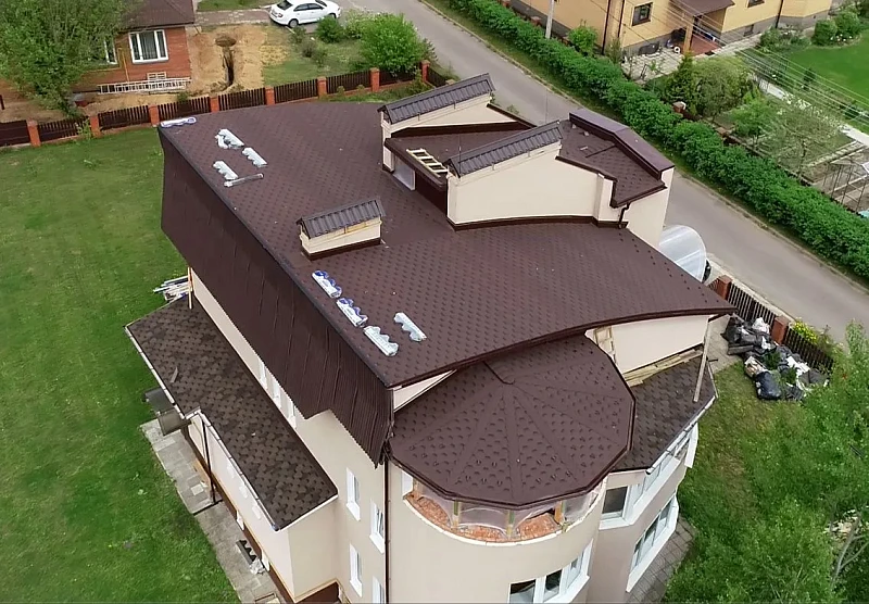 Вид сверху на кровлю коттеджа с гибкой черепицей и восьмигранной башней