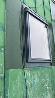 Мансардное окно в тёмной раме на зелёной металлической кровле, вид сбоку