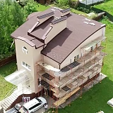 Фасад коттеджа с лесами во время монтажа кровли